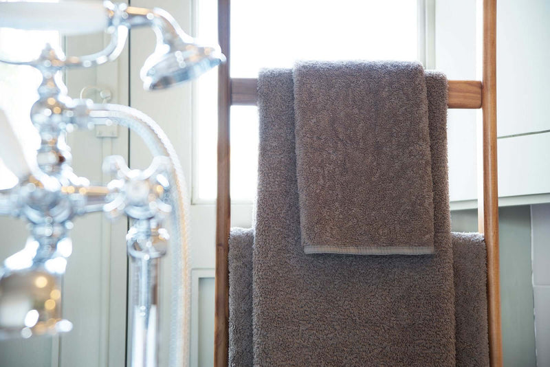 Luxus Handtücher in braunem Farbton aufgehängt über Holzstange, ideal für ein Badezimmer bei AmbientYou.com.