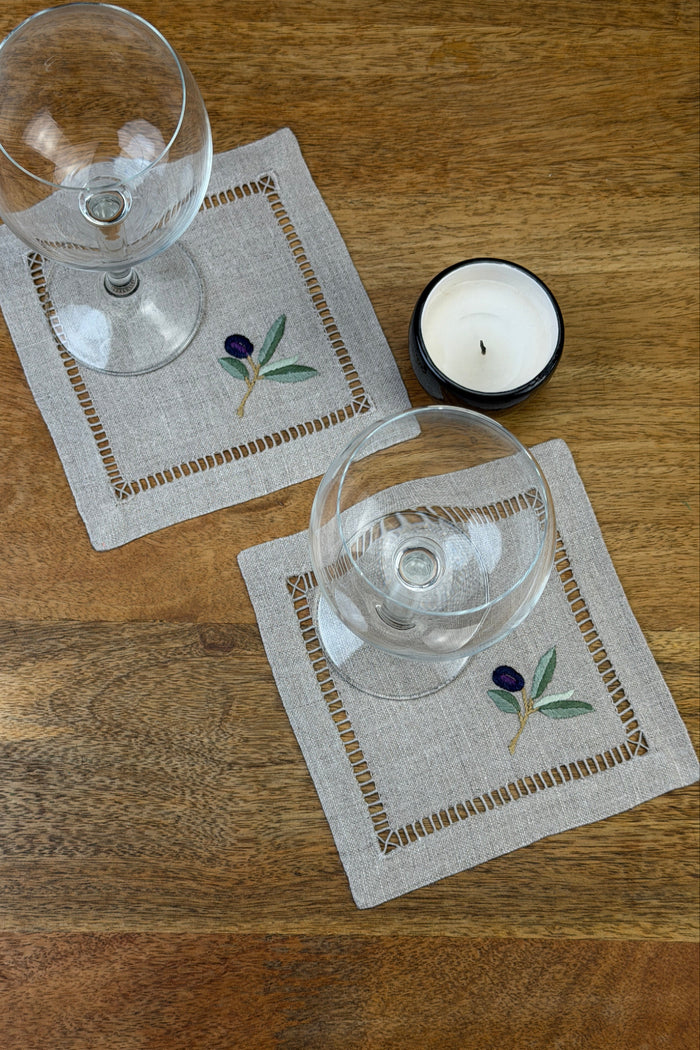 Zwei Cocktail Servietten Naturleinen 17x17cm mit Weingläsern und Teelicht auf einem Holztisch.