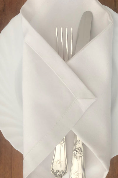 Servietten aus Stoff mit breitem Saum und mit silbernem Besteck dekoriert