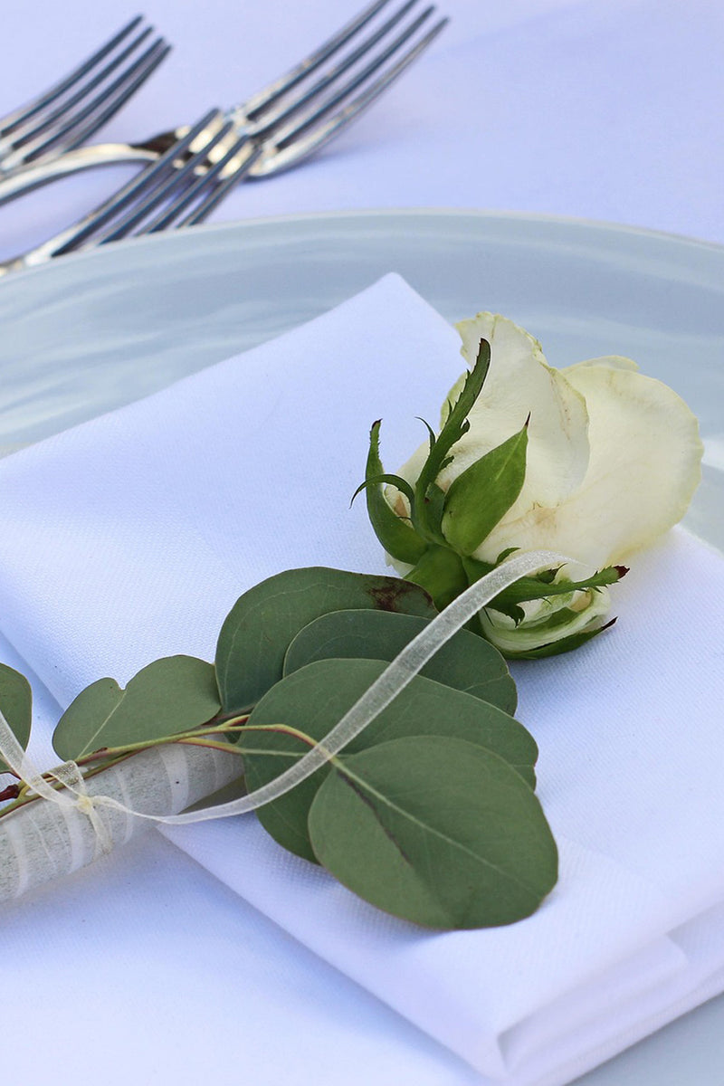 Servietten aus Stoff, breiter Saum, mit silbernem Besteck und einer weißen Rose dekoriert