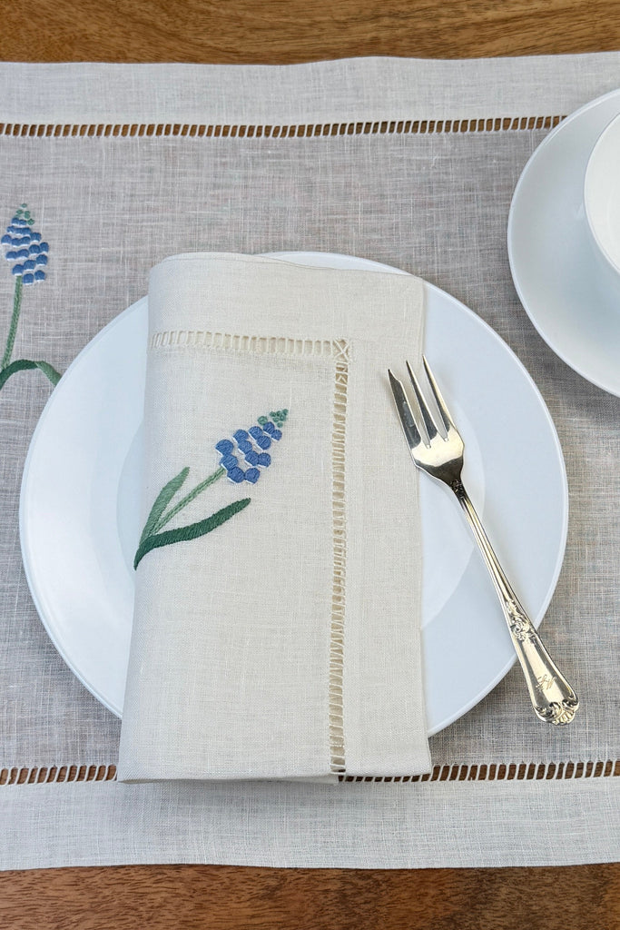 Leinenservietten mit Muscari handbestickt auf Teller und mit Tischset in Szene gesetzt.