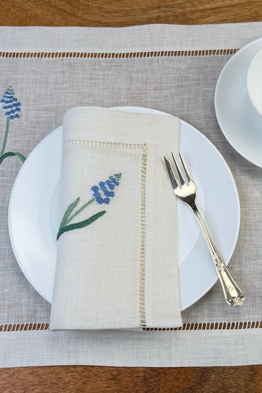 Leinenservietten mit Muscari handbestickt auf Teller und mit Tischset in Szene gesetzt.