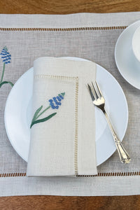 Leinenservietten mit Muscari handbestickt auf Teller und mit Tischset in Szene gesetzt.