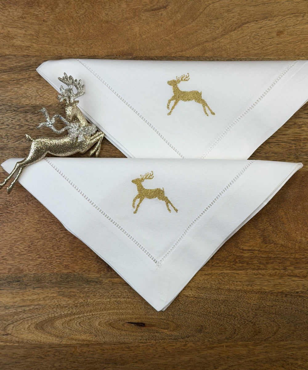 Stoffservietten Christmas Deer 50x50cm in Gold handgestickt mit Hohlsaum auf Holztisch dekoriert.