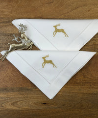 Stoffservietten Christmas Deer 50x50cm in Gold handgestickt mit Hohlsaum auf Holztisch dekoriert.