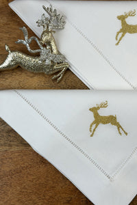 Stoffservietten Christmas Deer 50x50cm in Gold handgestickt mit Hohlsaum auf Holztisch dekoriert.