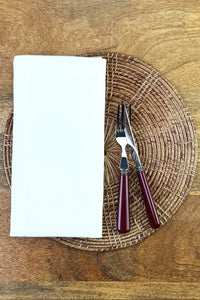 Stoffserviette Como auf geflochtenem runden Platzteller und weinrotes Bistrobesteck.