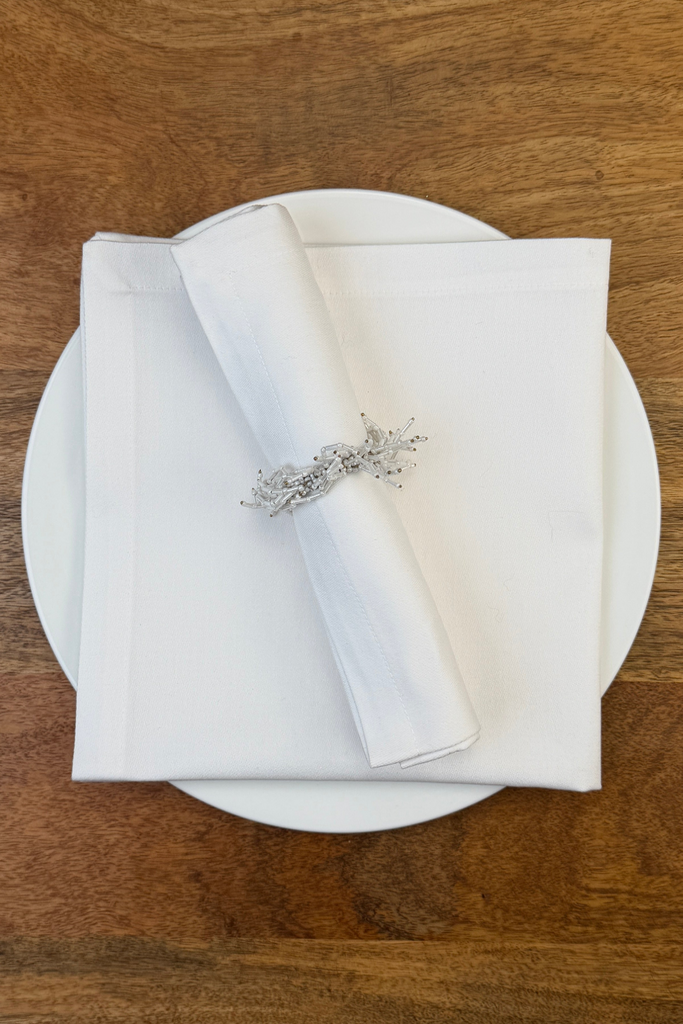 Stoffserviette Como mit Serviettenring auf Teller dekoriert.