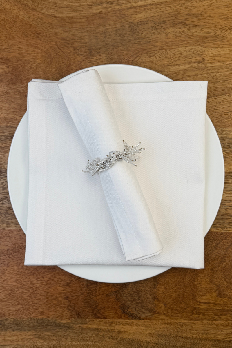 Stoffserviette Como mit Serviettenring auf Teller dekoriert.