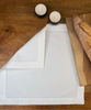 Stoffserviette Como weiss 45x45cm mit Hohlsaum und 4cm Bordüre auf Holztisch mit Holzbrett und Baguette. 