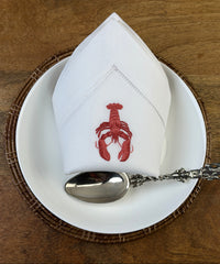 Stoffservietten Hummer 50x50cm handgestickt mit Hohlsaum auf Holztisch mit Löffel, Essteller und geflochtenem Untersetzer gedeckt.