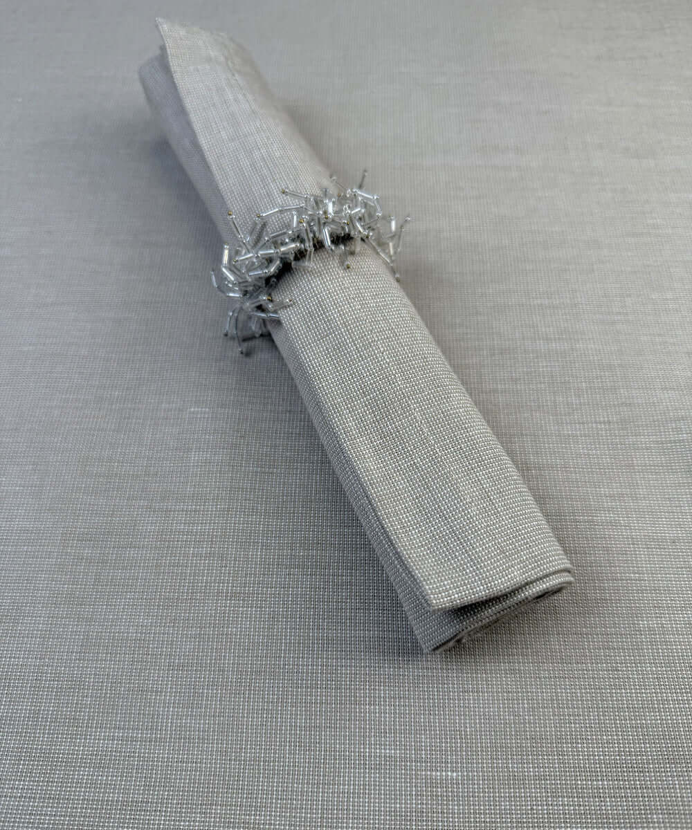 Stoffserviette Keitum 50x50cm Farbe Sand mit Serviettenring aus weißen Glasperlen.