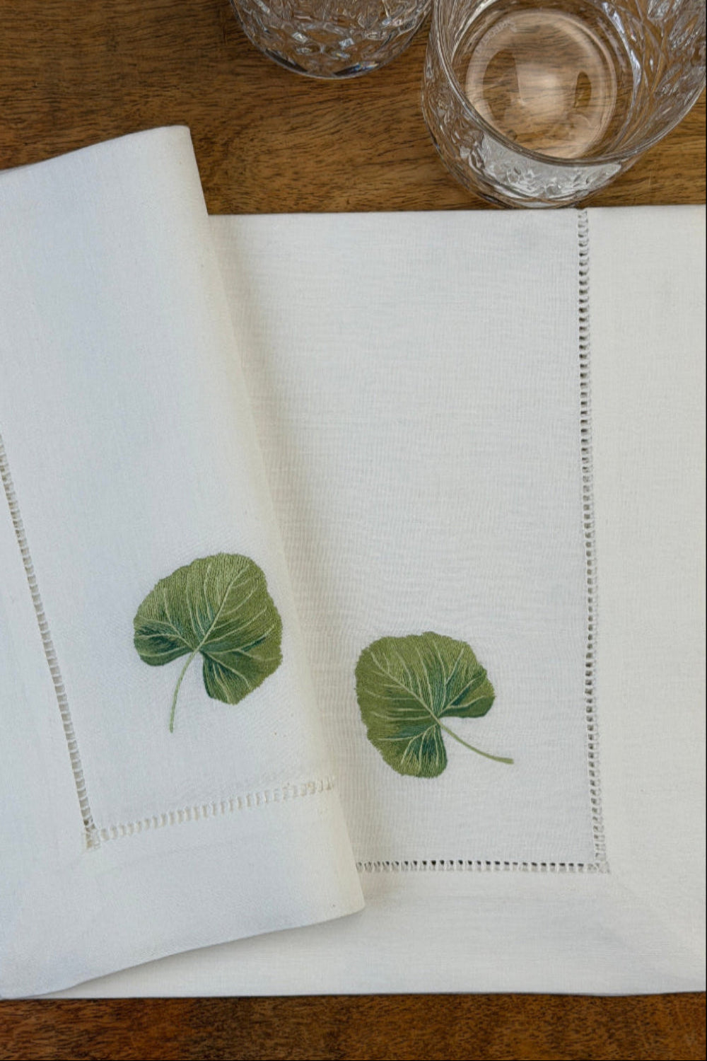 Stoffservietten Linde 50x50cm handgestickt mit Hohlsaum auf Holztisch mit Gläsern gedeckt.
