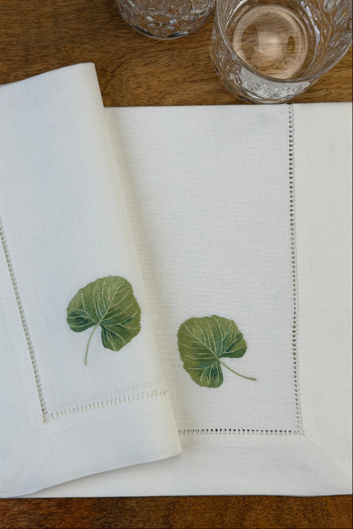 Stoffservietten Linde 50x50cm handgestickt mit Hohlsaum auf Holztisch mit Gläsern gedeckt.