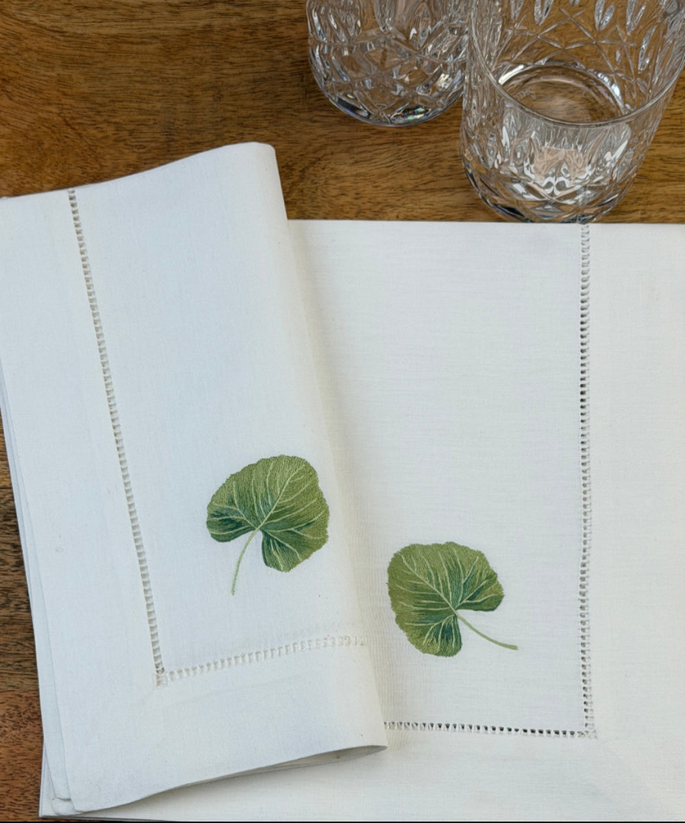Stoffservietten Linde 50x50cm handgestickt mit Hohlsaum auf Holztisch mit Gläsern gedeckt.