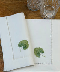 Stoffservietten Linde 50x50cm handgestickt mit Hohlsaum auf Holztisch mit Gläsern gedeckt.