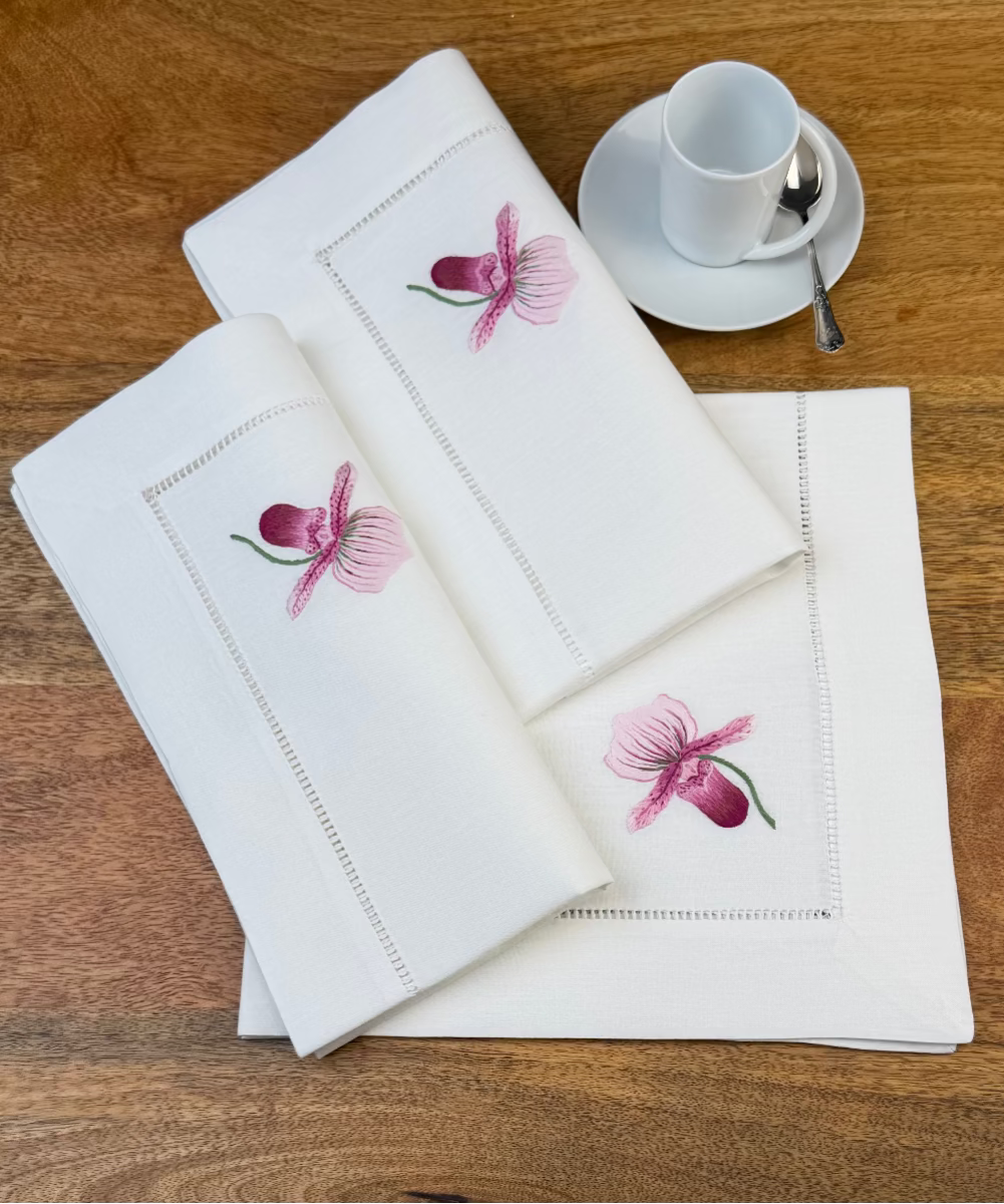 Stoffservietten Orchidee Rosa 50x50cm handgestickt mit Hohlsaum auf Holztisch mit Kaffeetass eingedeckt.