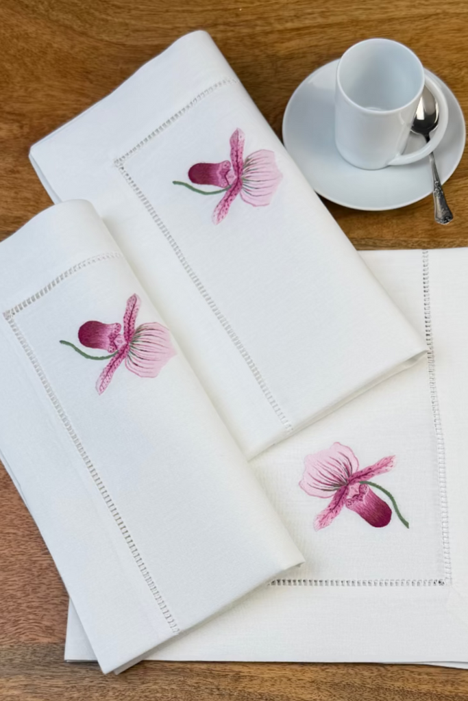 Stoffservietten Orchidee Rosa 50x50cm handgestickt mit Hohlsaum auf Holztisch mit Kaffeetass eingedeckt.