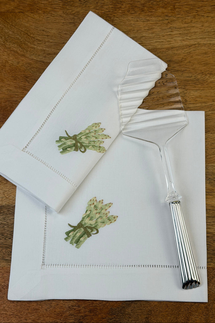 Stoffservietten Spargel 50x50cm handgestickt mit Hohlsaum auf einem Holztisch und mit einem Spargelheber dekoriert.