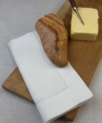 Stoffserviette Sylt 50x50cm weiß auf Holzbrett mit Baguette.