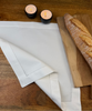 Stoffserviette Sylt weiß 45x45cm mit Hohlsaum auf Holztisch mit Holzbrett und Baguette.