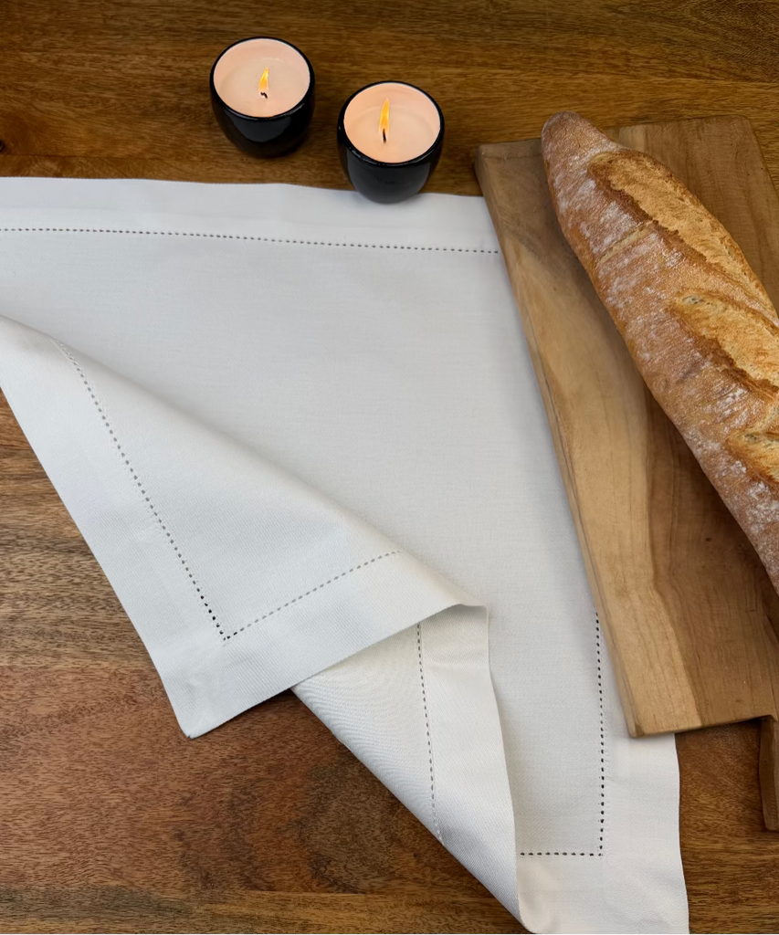 Stoffserviette Sylt weiß 45x45cm mit Hohlsaum auf Holztisch mit Holzbrett und Baguette.