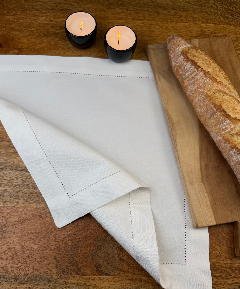 Stoffserviette Sylt weiß 45x45cm mit Hohlsaum auf Holztisch mit Holzbrett und Baguette.