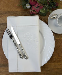 Stoffservietten Weiße Rose 50x50cm handgestickt mit Hohlsaum, dekoriert mit Blumenarrangement, Kaffeeservice und Kuchen Besteck auf Holztisch.