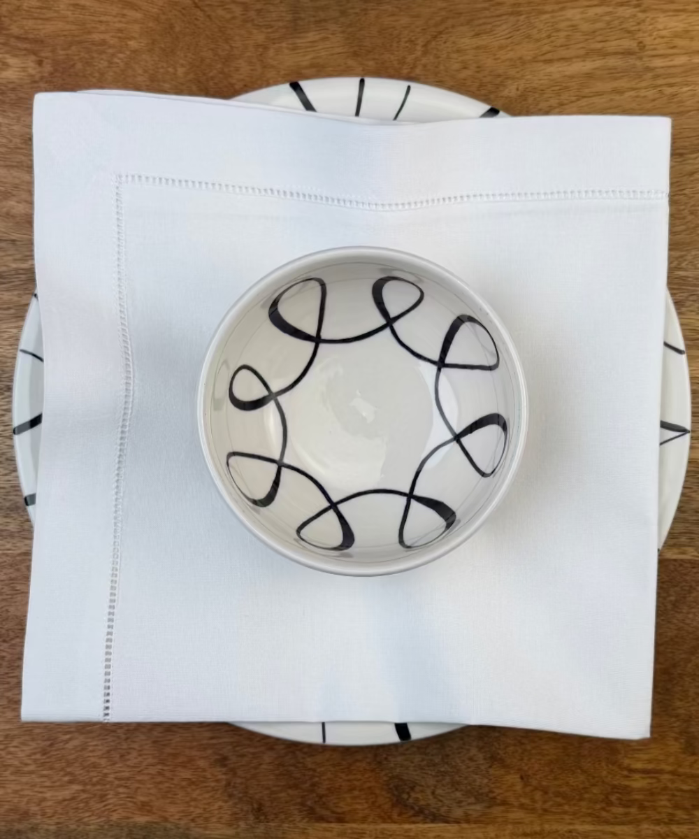 Stoffservietten weiss Toscana 50x50cm mit Hohlsaum dekoriert auf einem Essteller und Bowl auf Holztisch.