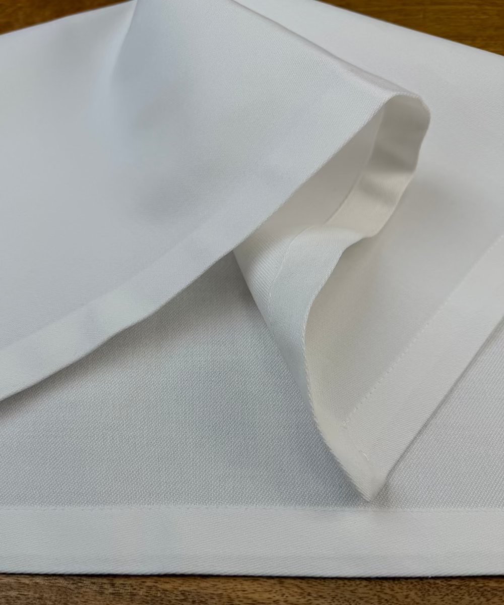 Stoffservietten Como weiß 50x50cm auf Holztisch drapiert.