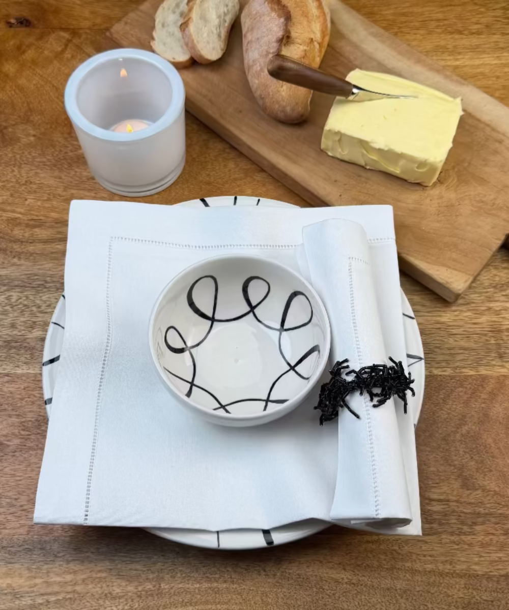 Zwei Stoffservietten weiss Toscana eine mit Perlen-Serviettenring mit Essteller und Brotzeit auf Holztisch. Es ist angerichtet.