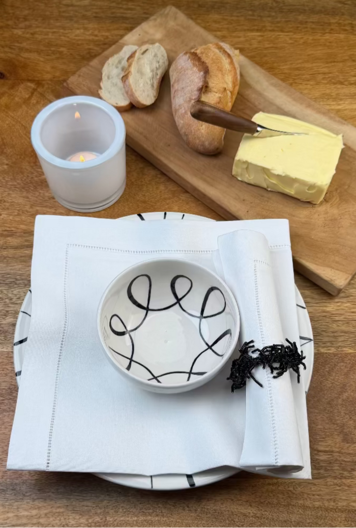 Stoffserviette weiss Toscana auf Holztisch mit Essteller, Bowl, Baguette und Butter.