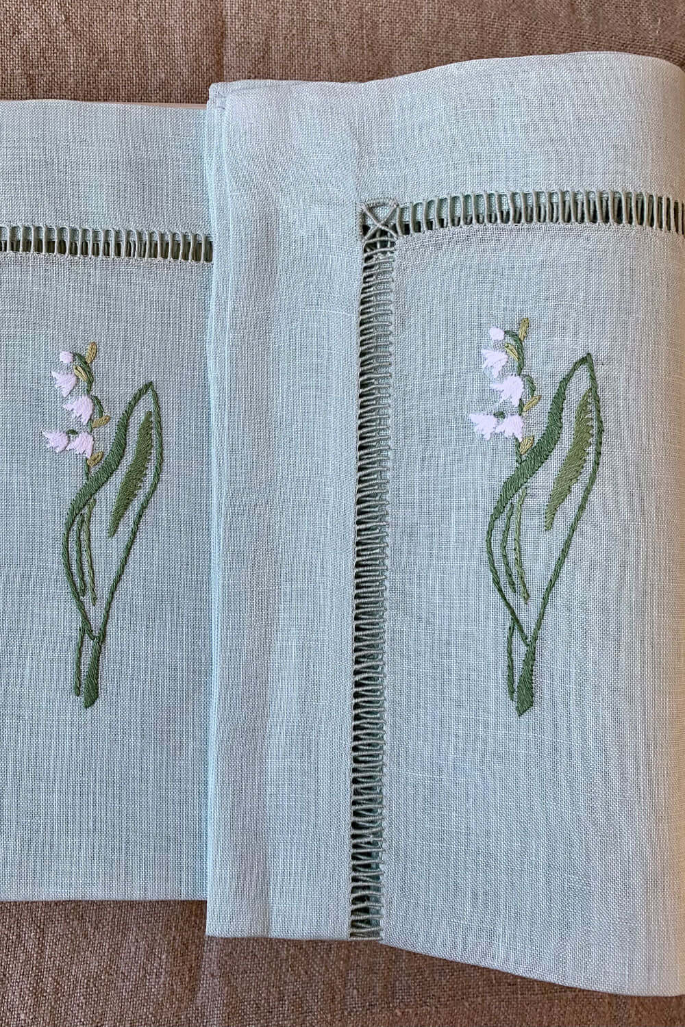 Leinenservietten bestickt mit Maiglöckchen auf zartem grünen Leinen für eine elegante Tischdekoration.