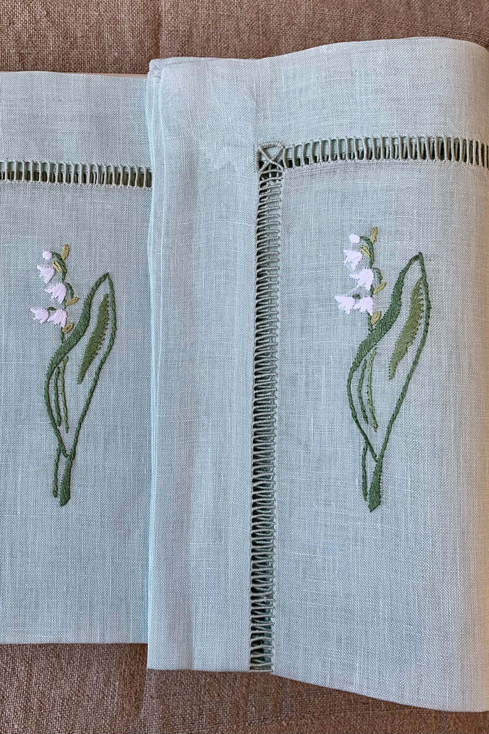 Leinenservietten bestickt mit Maiglöckchen auf zartem grünen Leinen für eine elegante Tischdekoration.
